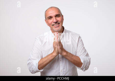 Closeup portrait of mature man désespérée en chemise blanche montrant les mains jointes,demander de l'aide ou une excuse. Banque D'Images