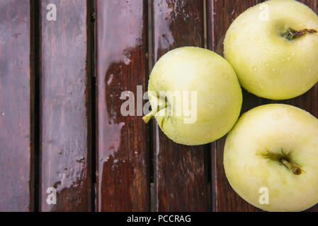 Close-up of golden humide quelques pommes vertes couvertes par les gouttes d'eau sur l'ancienne en bois naturel humide brun surface de la table. Arrière-plan avec des fruits mûrs et spa copie Banque D'Images