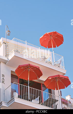 Façade moderne de café avec balcon et terrasse d'été avec trois parapluies rouges contre le ciel bleu clair, low angle view Banque D'Images