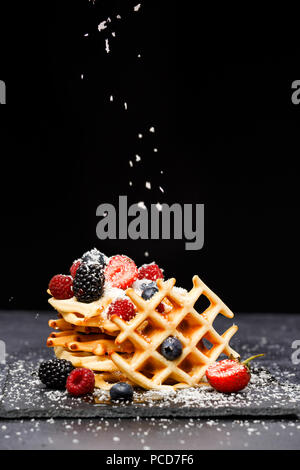 Photo de gaufres aux fruits rouges viennois frais saupoudrés de sucre en poudre sur tableau noir sur fond blanc Banque D'Images