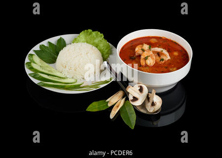 Tom Yum ou tom yam est un type de soupe Thaï aigre et piquante, généralement cuite avec des crevettes. Servi avec du riz, des légumes et des baguettes. Isolé sur re noir Banque D'Images