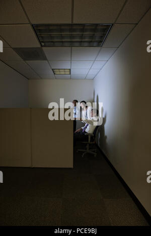 Une race mixte groupe de trois personnes d'affaires éclairés à l'écran d'un ordinateur de bureau dans un petit coin du bureau de l'armoire. Banque D'Images