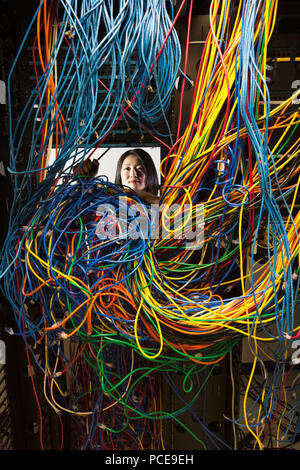 Asian female technician woking sur un enchevêtrement de câbles CAT 5 mess dans une salle serveur. Banque D'Images