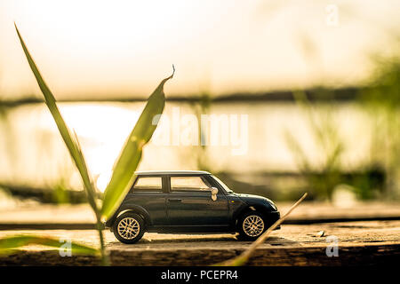 Voiture bleue sur socle bois sur fond coucher de soleil sur la rivière Banque D'Images