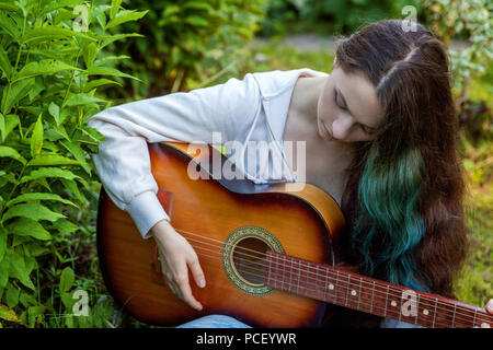 Jeune femme assise hipster dans l'herbe et jouer de la guitare sur parc ou jardin arrière-plan. Teen girl apprendre à jouer la chanson et de la musique. Passe-temps, de vie, de vous détendre, d'un instrument, l'éducation, loisirs concept Banque D'Images