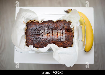 Vegan fait maison pain aux bananes cuites sur du papier parchemin juste hors du four sur une planche à découper blanc Banque D'Images