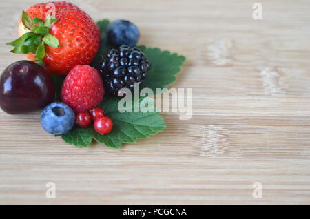 Détail de fruits frais, de baies. Fraises, framboises, cerises, mûres, myrtilles et groseilles rouges sur bamboo board with copy space Banque D'Images