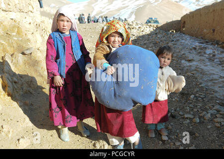 Le sergent de la Police nationale afghane. Mohammed Tahir, mains certains des vêtements d'hiver d'un jeune garçon à l'Aq Robat, un village éloigné à plus de 20 milles au nord-ouest de Bamyan, 24 décembre. Les vêtements ont été donnés par les soins de l'opération : l'Afghanistan, un organisme de bienfaisance sans but lucratif, privé basé à l'aérodrome de Bagram, en Afghanistan. L'ANP a travaillé avec des représentants des autorités locales et de l'armée américaine pour distribuer les éléments. Banque D'Images