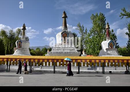 Lhassa, DANS LA RÉGION AUTONOME DU TIBET, CHINE - CIRCA MAI 2018 : promeneurs sur roues de prière tibétain avec trois stupas blancs dans l'arrière-plan. Banque D'Images