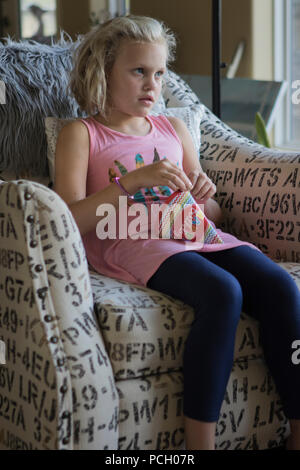 Jolie fille blonde de 8 ans, assis. dans une chaise, en pleine réflexion, à droite de l'appareil photo. Un éclairage doux. Communiqué de modèle # 113 Banque D'Images