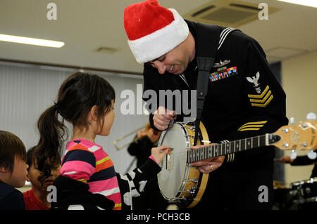 YOKOSUKA, Japon (déc. 3, 2012) 1ère classe Nefferdorf Musicien Brian, un membre de la 7ème Flotte américaine en Extrême-Orient Edition Brass Band, permet à un enfant de strum son banjo au cours d'une exécution musicale de Noël au Sullivans Elementary School à Yokosuka, activités de la flotte de commandement. Le groupe joue la musique à plusieurs endroits tout au long de la journée y compris le Centre de développement de l'enfant et à l'extérieur de l'échange de la Marine. Banque D'Images