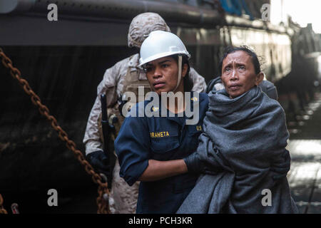 Détroit de Makassar (10 juin 2015) Un marin prend une femme de personnel médical à bord du navire de débarquement quai amphibie USS Rushmore (LSD 47). Rushmore a secouru 65 personnes d'un naufrage de plaisance dans l'océan pacifique entre les îles indonésiennes de Kalimantan et Sulawesi. Une fois à bord, les individus ont été secourus a fourni de la nourriture et des soins médicaux par les Marines et les marins de la 15e unité expéditionnaire de marines et de l'Essex groupe amphibie. Banque D'Images