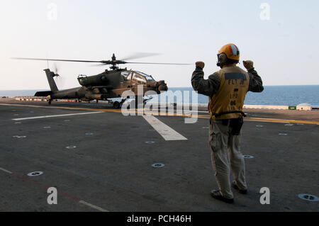 Un marin américain dirige les pilotes d'une armée AH-64D Longbow Apache helicopter affecté à la 4e Bataillon de reconnaissance aérienne de l'aviation de combat, 2e Brigade, 2e Division d'infanterie à la terre à bord du navire d'assaut amphibie USS Bonhomme Richard (DG 6) dans la mer de Chine orientale, le 11 avril 2014. Le Bonhomme Richard était en cours aux États-Unis 7e flotte domaine de responsabilité des opérations de sécurité maritime et les efforts de coopération en matière de sécurité dans le théâtre. Banque D'Images