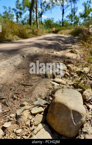 Un enfant marche dans une route poussiéreuse à sec à travers un paysage sec chaud, Townsville, Queensland, Australie Banque D'Images