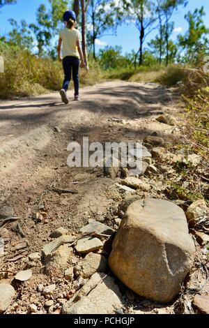 Un enfant marche dans une route poussiéreuse à sec à travers un paysage sec chaud, Townsville, Queensland, Australie Banque D'Images