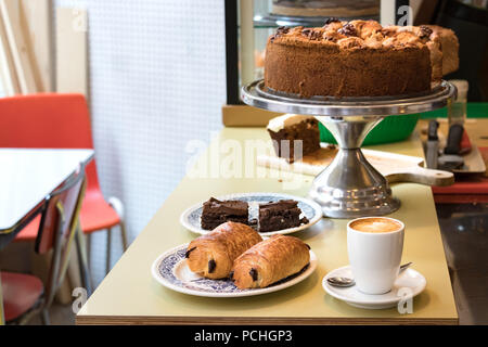 Une plaque avec deux pains au chocolat, une tasse de café expresso, bownies et une tarte aux pommes hollandaise avec les écrous sur le dessus, le tout sur une table en bois, à l'intérieur. Banque D'Images