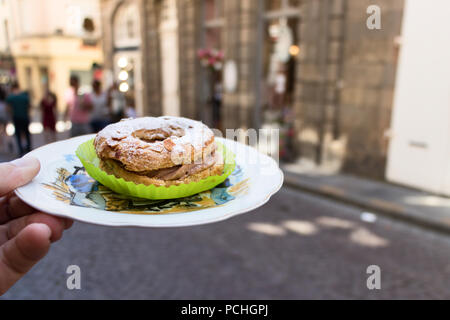 Une main tenant un homme Paris - Brest place de gâteau sur une plaque sur une rue arrière-plan flou. Banque D'Images