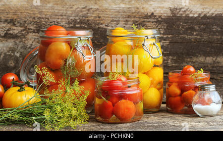 Tomates Marinées dans des bocaux sur table en bois . Processus de fermentation les tomates en pots de verre variété - rouge jaune, orange Banque D'Images