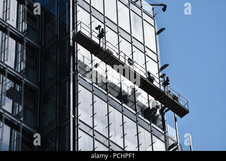 Travailleurs de la construction sur une plate-forme suspendue sur un gratte-ciel à la façade de verre Banque D'Images