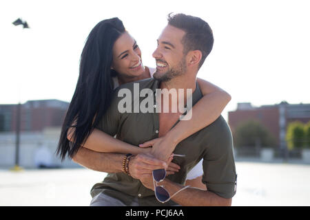 Happy young woman embracing man élégant de l'arrière à l'extérieur dans le coucher du soleil, piggyback ride Banque D'Images