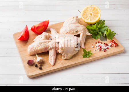 Ailes de poulet crues dans la marinade avec la sauce, le poivre et les verts sur support en bois. Focus sélectif. Banque D'Images