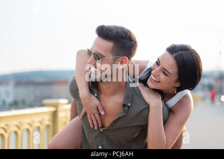 Happy young woman embracing man élégant de l'arrière à l'extérieur dans le coucher du soleil, piggyback ride Banque D'Images