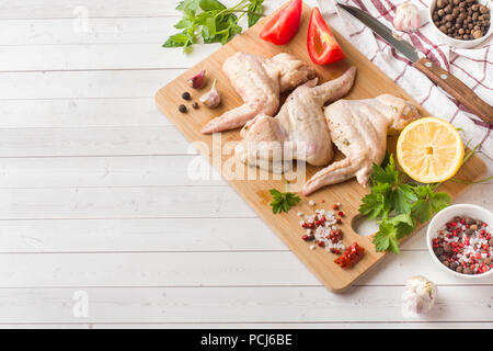 Ailes de poulet crues dans la marinade avec la sauce, le poivre et les verts sur support en bois. Focus sélectif. Banque D'Images