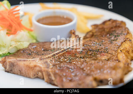 L'aloyau grillé tendre ou t-bone steak servi avec des frites dorées et salade d'herbes fraîches accompagnées de sauce ketchup poivre noir. Banque D'Images