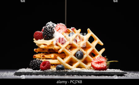 Photo de gaufrettes viennoises avec framboises, fraises saupoudrées de sucre en poudre, avec du miel sur fond vide noir Banque D'Images