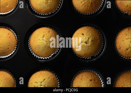 Coup de frais généraux de cuisson noir rempli de petits gâteaux fraîchement préparés dans le cas du papier visible avec le mélange à gâteau avec spaltters et coulures. Banque D'Images