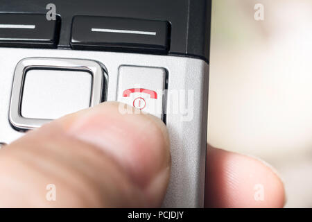 Homme doigt sur le bouton Raccrocher rouge d'un Telefphone DECT sans fil, prêt à mettre fin à l'appel Banque D'Images