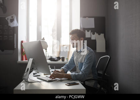 Jeune mâle concepteur à l'aide de tablette graphique tout en travaillant avec com Banque D'Images