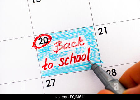 Stylo avec les doigts femme rappel écrit de nouveau à l'école dans le calendrier. Close-up. Banque D'Images