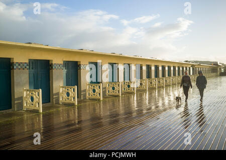 Un couple marcher leur chien le long de la promenade des Planches humides cours des cabines de plage à Deauville, Normandie, France après une douche de pluie Banque D'Images