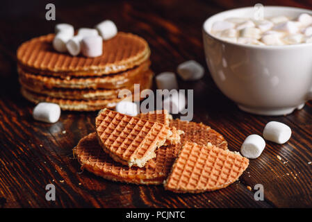 Avec une rupture Stroopwafel avec blanc tasse de cacao avec de la guimauve et Waffle pile sur toile. Banque D'Images