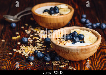Petit-déjeuner sain avec Granola, banane, myrtille et du yaourt grec. Ingrédients éparpillés sur la table en bois. Banque D'Images
