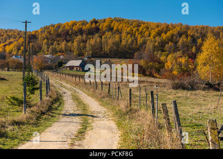 Route de terre par l'intermédiaire de village de montagne. Autumn Forest et maison en bois Banque D'Images