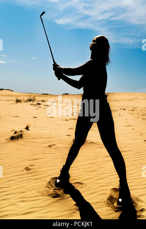 Silhouette d'une femme avec les cheveux volant en jouant au golf dans le désert Banque D'Images