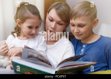 Belle mère est en train de lire un livre à ses jeunes enfants. Soeur et frère est l'écoute d'une histoire. Banque D'Images