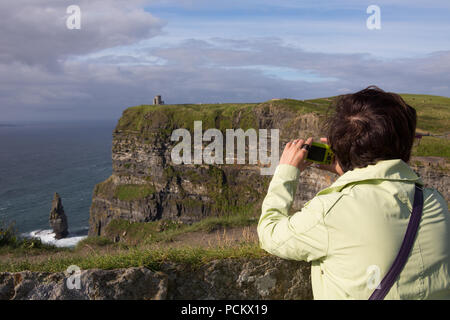 Une femme prend une photo sur les falaises de Moher, comté de Clare, Irlande Banque D'Images