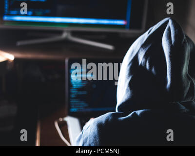Hacker in hoodie tapant code de program using laptop in the studio Banque D'Images