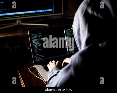 Hacker in hoodie tapant code de program using laptop in the studio Banque D'Images