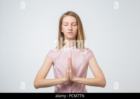 Le yoga et la méditation. Jeune femme habillée avec désinvolture européenne en gardant les yeux fermés tout en méditant, détendre durant dure journée de travail au bureau, ho Banque D'Images