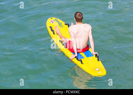 Bournemouth, Dorset, Royaume-Uni. 3 août 2018. Météo au Royaume-Uni : les foules affluent en bord de mer pour profiter du temps chaud et ensoleillé sur les plages de Bournemouth. RNLI Lifeguard gardant un regard dehors assis sur surf surf planche dans la mer. Crédit : Carolyn Jenkins/Alay Live News Banque D'Images