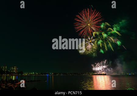 D'artifice multicolores au-dessus de l'océan dans la grande ville, les silhouettes des gens sur la plage, les bâtiments modernes sur l'arrière-plan, ardent et réflexion Banque D'Images