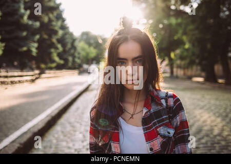 Portrait de superbe jeune femme avec calme en face de la lumière du soleil. Teen girl wearing plaid shirt rouge debout sur l'pavée à Banque D'Images