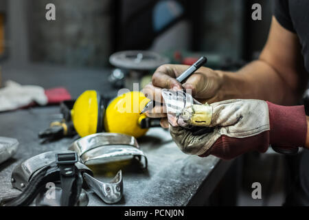 Travailleur de la construction métallique mâle et l'assemblage de pièce d'armure médiévale. Les mains de l'homme travaillant avec les pièces métalliques du matériel dans un atelier Banque D'Images