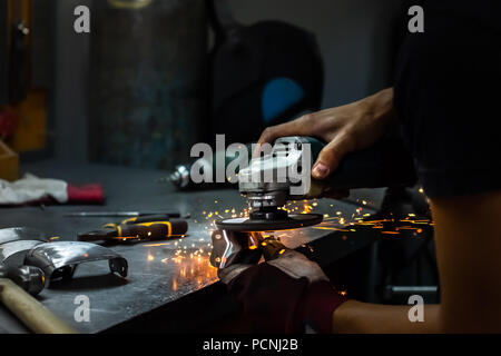 Homme travailleur et polissage métal finaliser pièce d'armure médiévale. Les mains de l'homme le traitement de pièces métalliques de matériel dans un atelier avec une meuleuse d'angle Banque D'Images