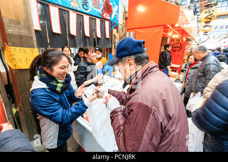 Kuromon Ichiba, marché alimentaire à Osaka. Avec blocage poissonnier senior male customer handing over billet pour le sac en plastique de smiling woman shop assistant Banque D'Images