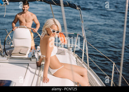 Belle jeune femme en bikini d'avoir le soleil tout en son petit ami yacht de direction Banque D'Images